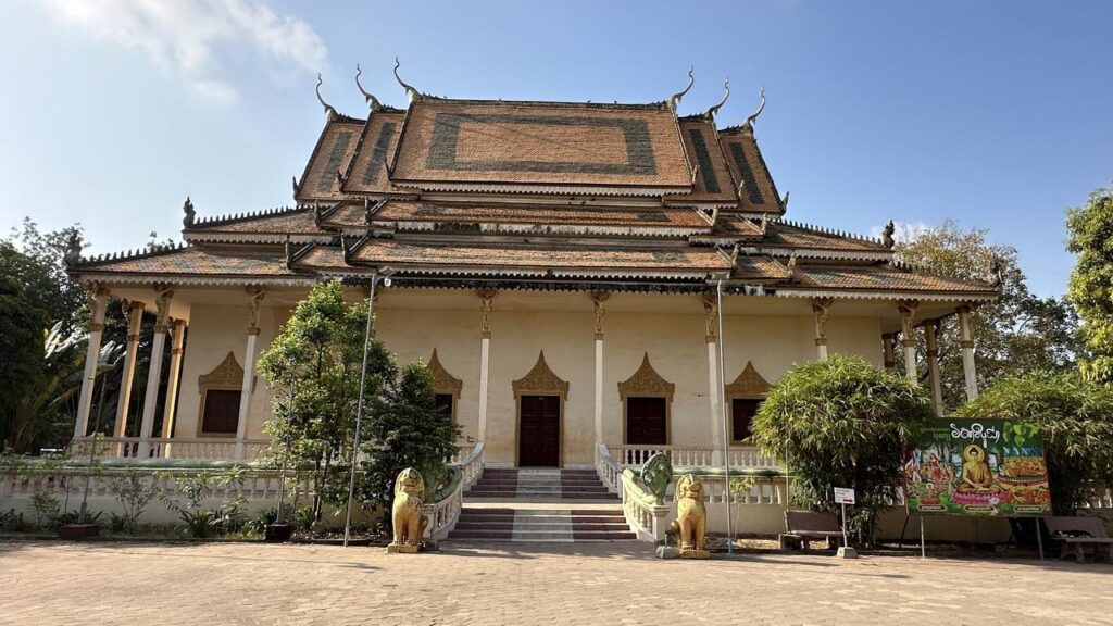 Ein traditioneller Buddhistentempel mit prächtigem Dach, Löwenstatuen und viel Grün unter locker bewölktem Himmel.