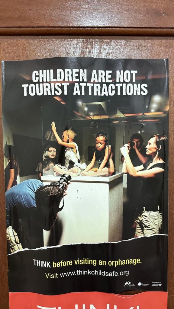 Auf dem Plakat sitzen Kinder in einer Glasvitrine, während Touristen Fotos machen. Die Botschaft: Kinder sind keine Attraktionen.