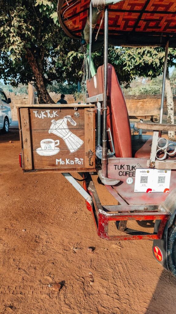 Ein Tuk Tuk mit liebevoll gemaltem Moka-Kännchen und Kaffeetasse parkt als "Tuk Tuk Moka Pot" unter Bäumen im Khmer-Reich.