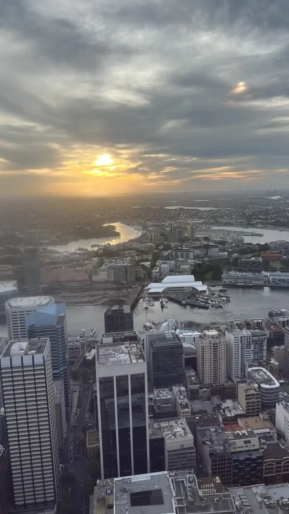 Stimmungsvolle Luftaufnahme einer Stadt mit Hochhäusern, Fluss und Sonnenuntergang, dessen Licht alles in warmen Farben taucht.
