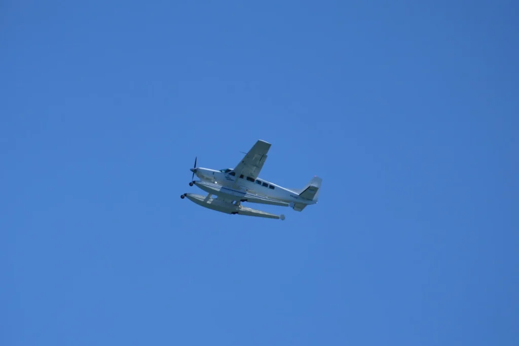 Ein weißes Wasserflugzeug mit Schwimmern gleitet freundlich durch den strahlend blauen Himmel - ein wunderschöner Anblick!.