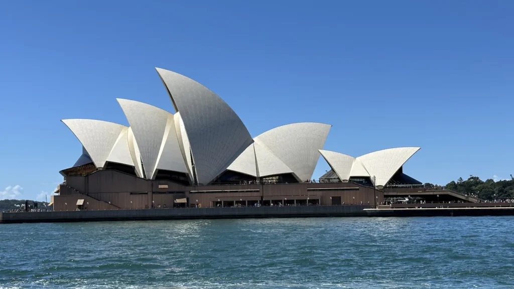 Das Sydney Opera House mit seinen weißen Segeldächern vor blauem Himmel und Wasser - ein wunderschöner Anblick am Hafen!.