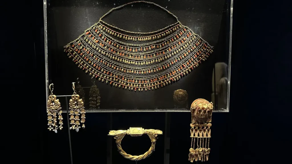 In einer Vitrine funkeln eine breite, verzierte ägyptische Halskette, goldene Ohrringe, ein Armreif und ein goldener Haarschmuck.