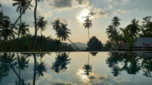 Palmen und Wolken spiegeln sich in einem ruhigen Pool bei Sonnenuntergang, dahinter Berge – Asien-Urlaubsfeeling pur.