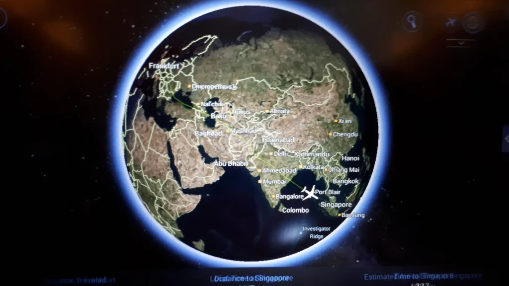 Ein digitales Display zeigt eine Flugkarte der Erde, auf der die Länder Europas, des Nahen Ostens und Asiens markiert sind. Die Flugroute ist eingezeichnet und wichtige Städte wie Singapur, Bangkok, Istanbul und die Neuseeländische Südinsel sind eingezeichnet.