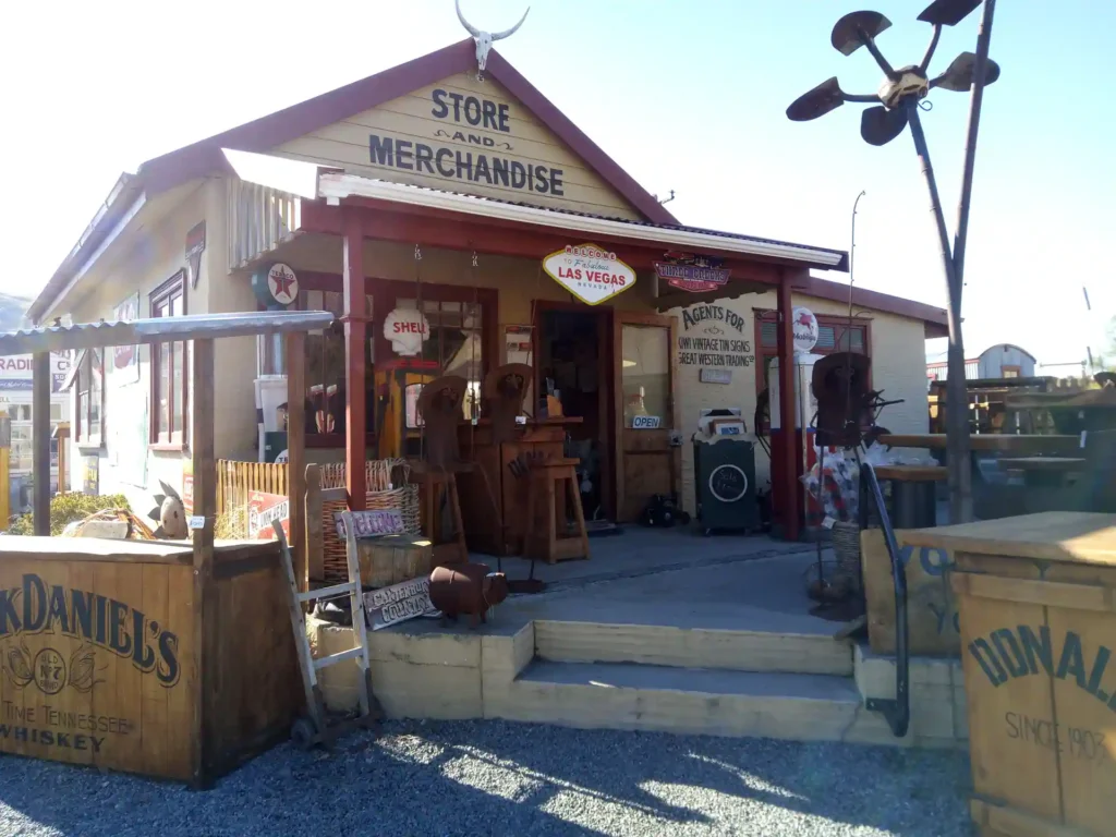 Ein rustikaler Laden mit einem Schild mit der Aufschrift "Store and Merchandise" erinnert an den altmodischen Western-Look der Neuseeland Südinsel. Alte Gegenstände, Schilder und Fässer schmücken die Veranda mit Holzstühlen und roter Dekoration.